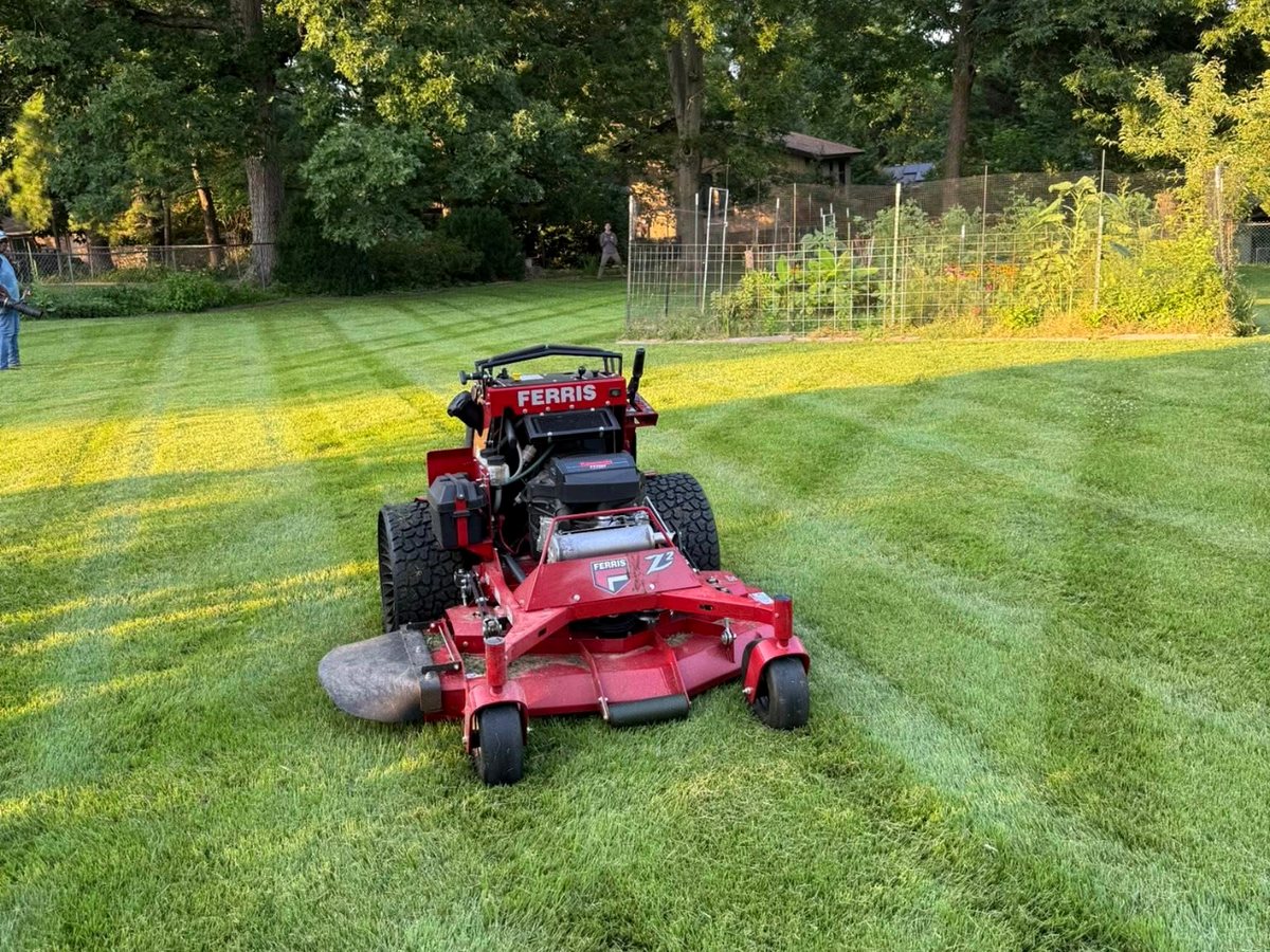 Commercial stand-on mower cutting stripes into a large lawn